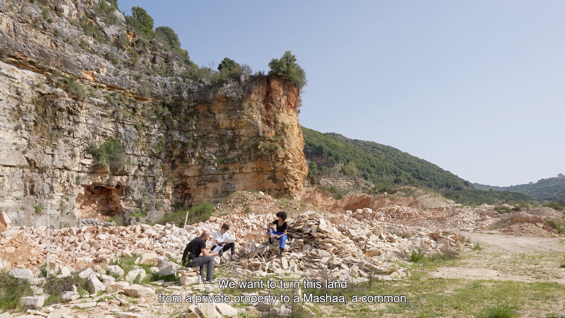 A rocky outcropping with three figures sitting beneath. 